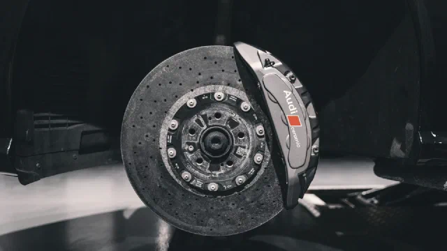 A large fixed brake caliper clamped over a drilled disc behind a wheel